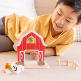 Child playing with the PlanToys barn house small world play set, holding the farmer figure up to the op window on the red barn.