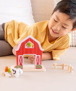 Child playing with the PlanToys barn house small world play set, holding the farmer figure up to the op window on the red barn.
