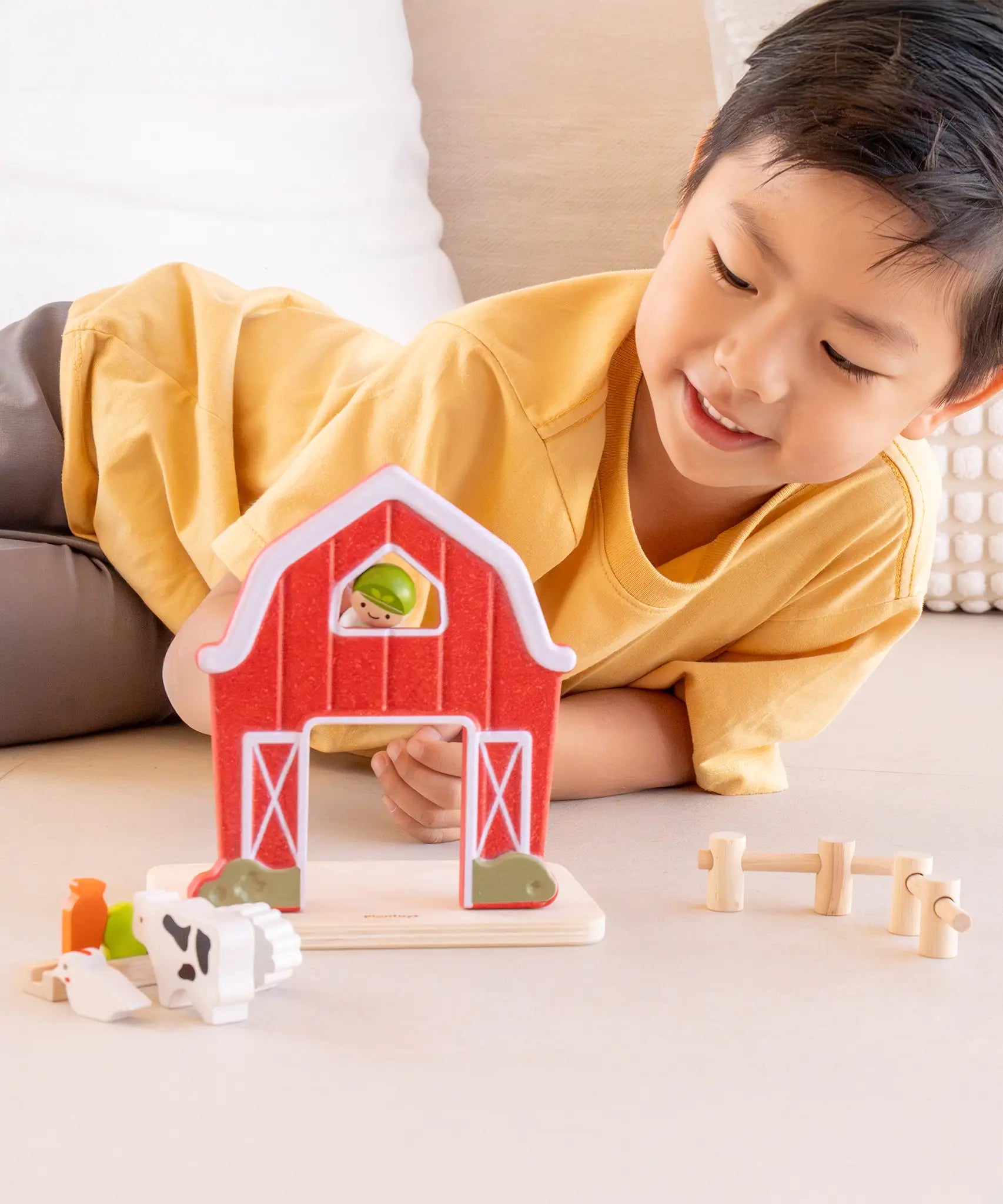 Child playing with the PlanToys barn house small world play set, holding the farmer figure up to the op window on the red barn.