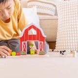 Child playing with the PlanToys barn house small world play set. Red wooden barn, mini veg patch, fences, cow, sheep, hen and farmer figure. 