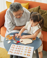Young girl and woman sat at a round table playing with the PlanToys wooden build a face toy