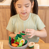 Child sitting at the table with a wooden avocado from the PlanToys chef salad bowl filled with play food
