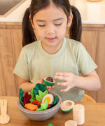 Child sitting at the table with a wooden avocado from the PlanToys chef salad bowl filled with play food