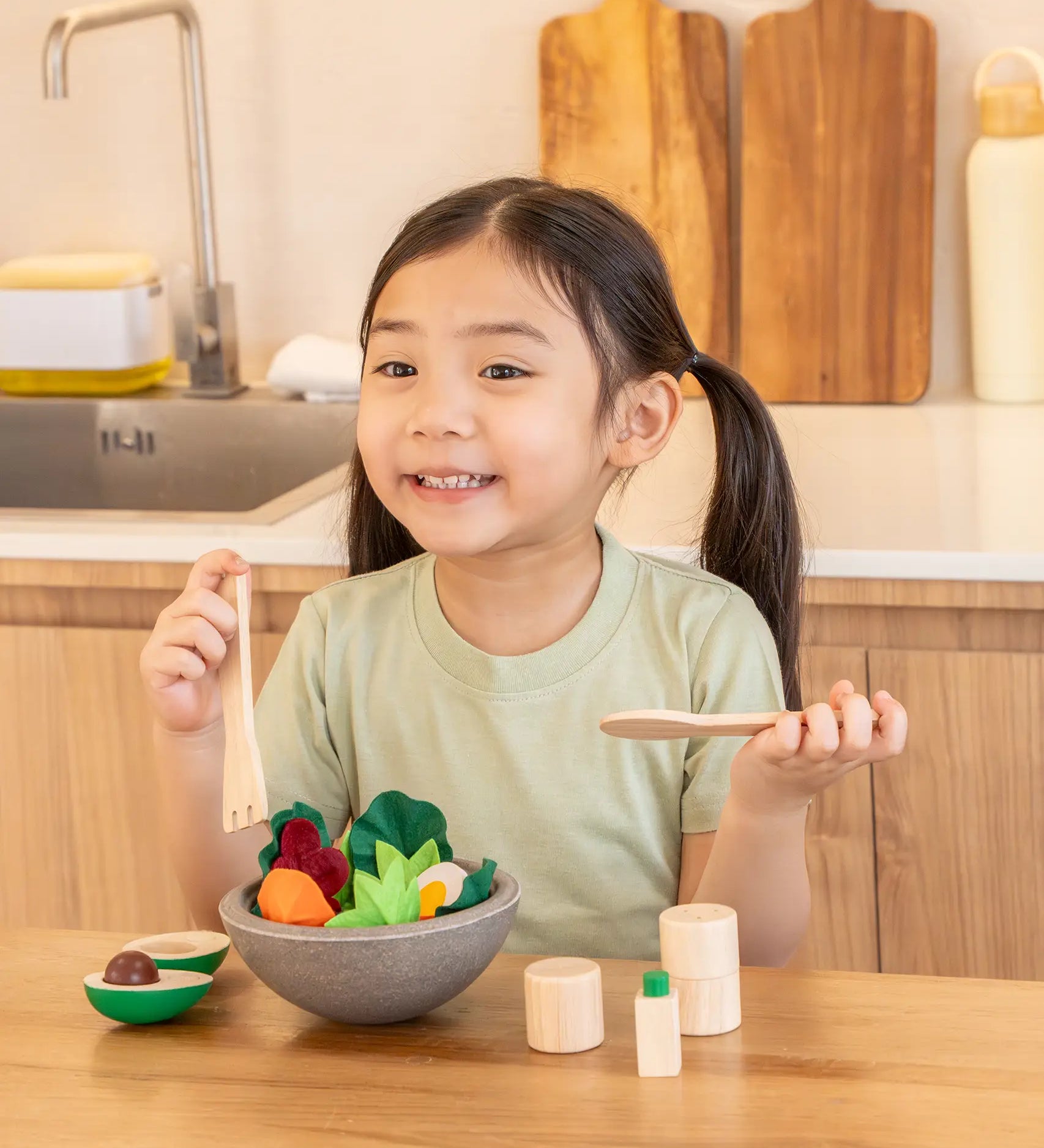 Child sitting at the table with a PlanToys chef salad bowl full of loose play food