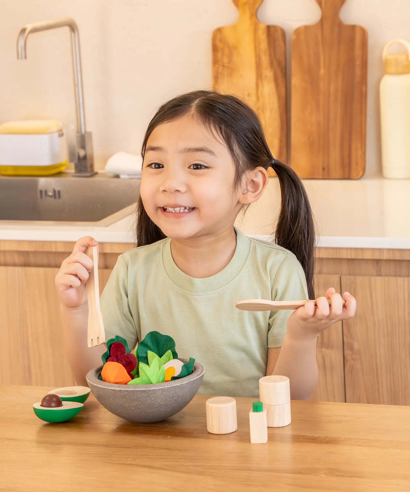 Child sitting at the table with a PlanToys chef salad bowl full of loose play food