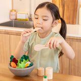 Child holding a wooden fork and spoon from the PlanToys chef salad bowl full of loose play food