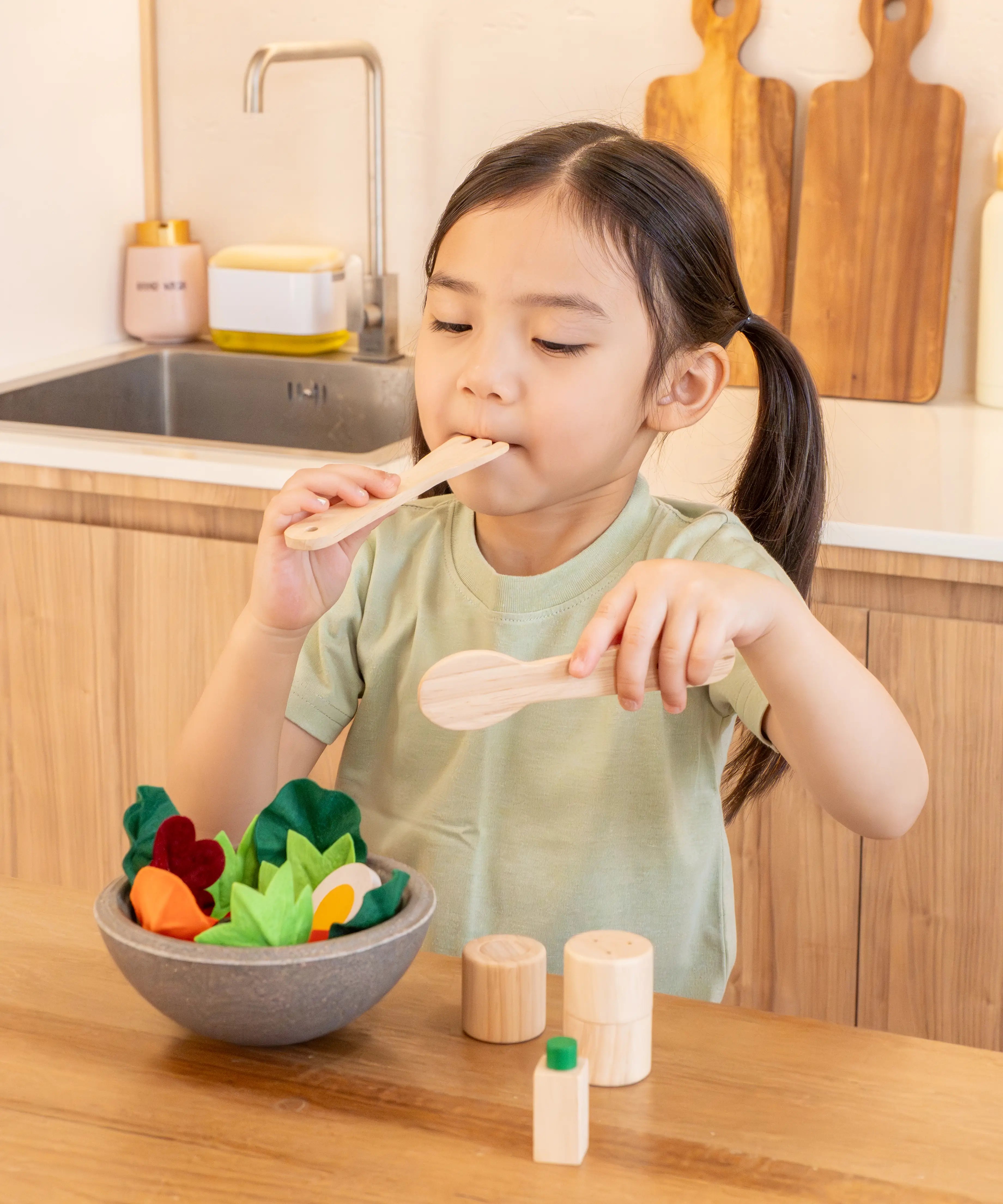 Child holding a wooden fork and spoon from the PlanToys chef salad bowl full of loose play food