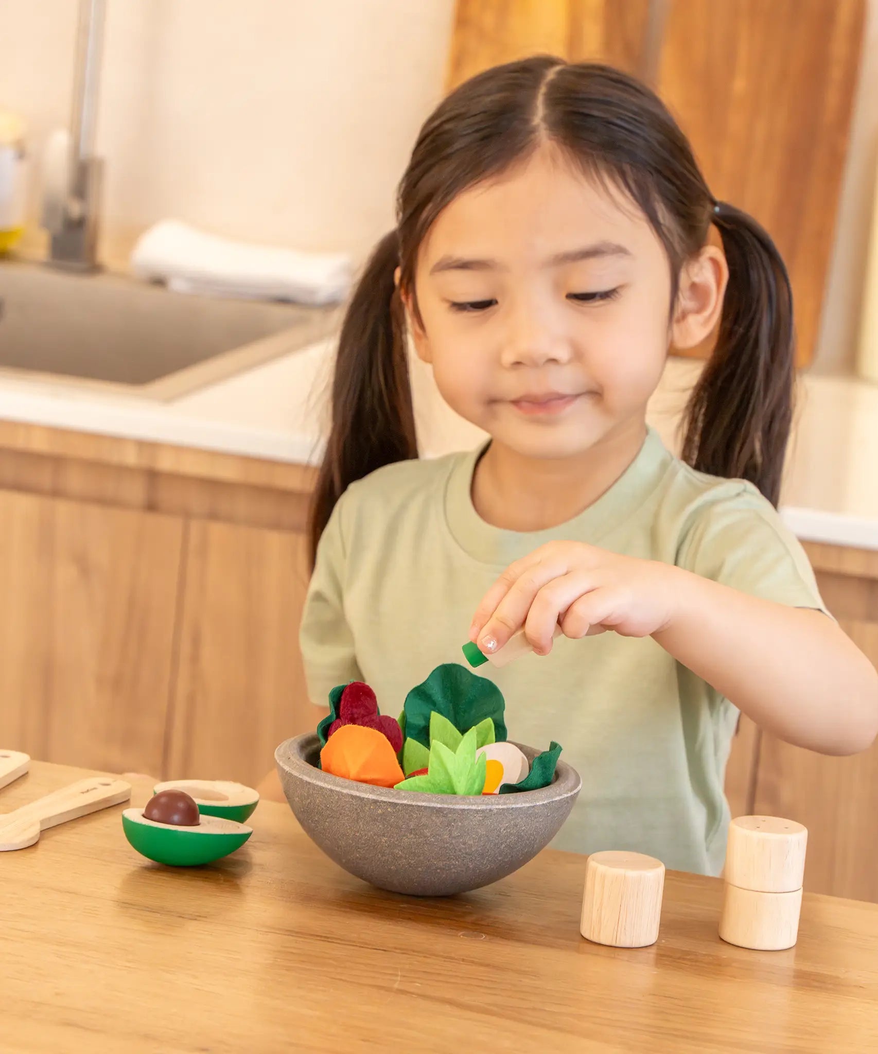 Child playing with the PlanToys chef salad bowl full of loose play food at the table