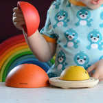 A child playing with the PlanToys Chicken Nesting Toy. A Grimm's rainbow can be seen behind them. 
