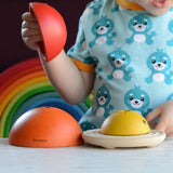 A child playing with the PlanToys Chicken Nesting Toy. A Grimm's rainbow can be seen behind them. 