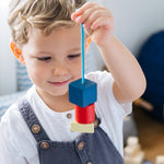 Close up of a child holding up some wooden PlanToys geo lacing blocks in front of his face