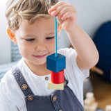 Close up of a child holding up some wooden PlanToys geo lacing blocks in front of his face