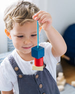 Close up of a child holding up some wooden PlanToys geo lacing blocks in front of his face