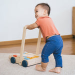 Young toddler walking around holding the Plan Toys eco-friendly wooden baby walker