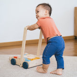 Young toddler walking around holding the Plan Toys eco-friendly wooden baby walker