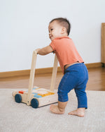 Young toddler walking around holding the Plan Toys eco-friendly wooden baby walker