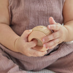 Young toddler sat on a white bed holding the PlanToys wooden sensory tumbling balls