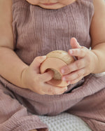 Young toddler sat on a white bed holding the PlanToys wooden sensory tumbling balls