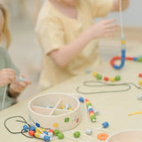 Children threading beads onto laces from the PlanToys threading beads wooden lacing toy. The wooden storage box is in front of them.