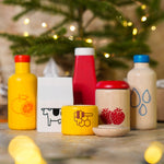 Close up of the PlanToys plastic-free wooden food and beverage play set in front of a small Christmas tree