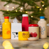 Close up of the PlanToys plastic-free wooden food and beverage play set in front of a small Christmas tree