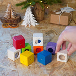 Close up of hand grabbing a white block from the PlanToys kids wooden sensory activity blocks in front of a small Christmas tree.