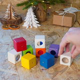 Close up of hand grabbing a white block from the PlanToys kids wooden sensory activity blocks in front of a small Christmas tree.