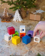 Close up of hand grabbing a white block from the PlanToys kids wooden sensory activity blocks in front of a small Christmas tree.