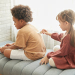 Girl drawing on a young boys back with the PlanToys wooden touch and guess game on a grey sofa