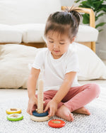 Child sat on a white carpet playing with the PlanToys plastic-free wooden sorting and stacking game