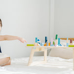 Young girl sat on a white bed pointing at the PlanToys eco-friendly wooden city blocks toy set