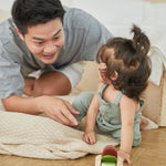 Young girl and man laying on a blanket playing with the PlanToys modern rustic plastic-free baby car toy