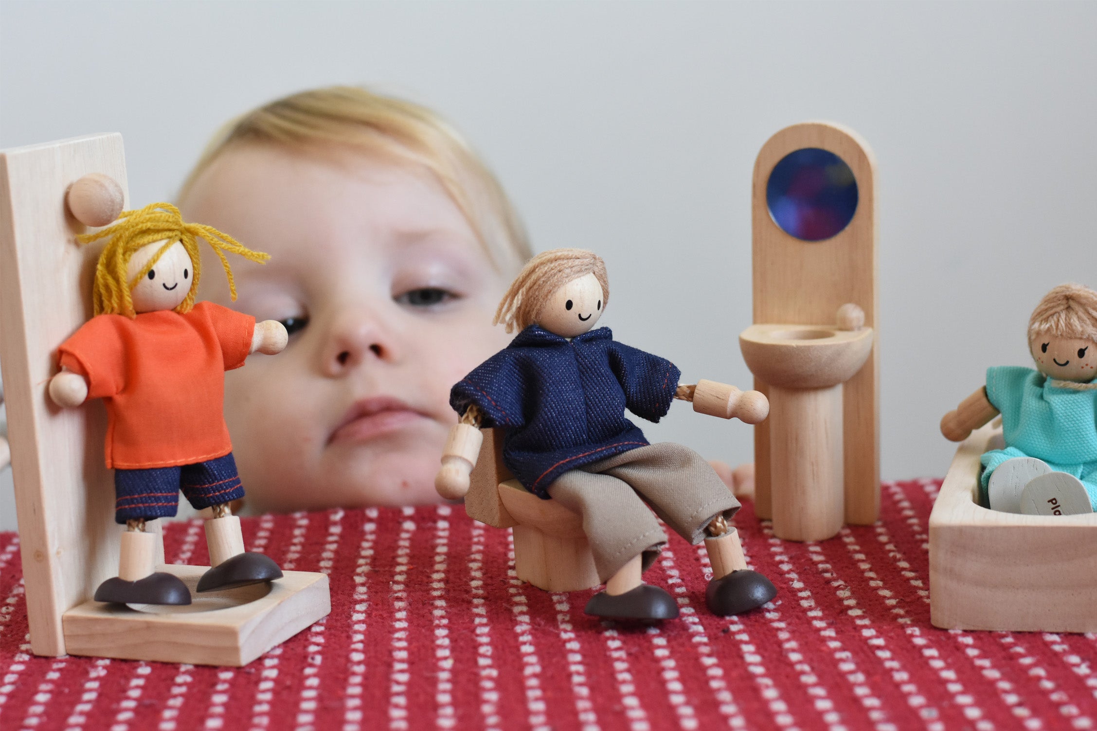 A child playing with peg dolls and the PlanToys classic natural wooden dollshouse bathroom furniture.