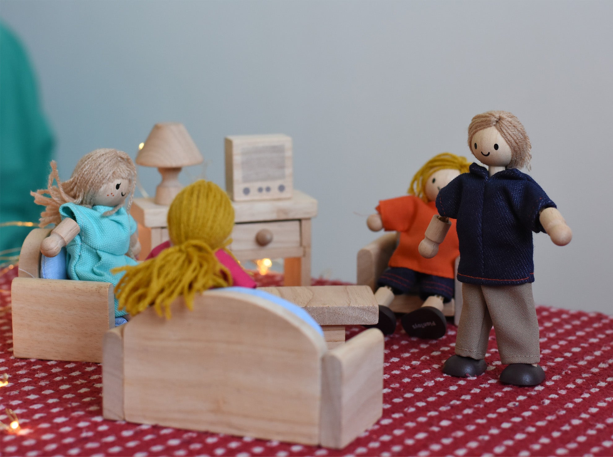 A play scene including PlanToys peg dolls sitting in their natural wooden living room furniture