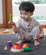 A child sitting on a grey coloured rug playing with the PlanToys Coloured Sorting Cones. 
