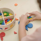 Close up of child's hand placing pieces from the PlanToys mosaic set into a circle shape. Brightly coloured wooden pieces in a storage box.