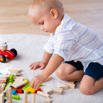 A child sat on a light grey coloured rug playing with the PlanToys 40 unit Colourful Block set. 