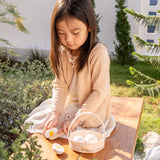 Child cutting a PlanToys wooden egg on a wooden table in the garden next o a basket full of other eggs