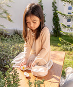 Child cutting a PlanToys wooden egg on a wooden table in the garden next o a basket full of other eggs