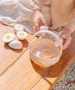 Child holding a Plantoys wooden play egg above a fabric basket on a wooden bench