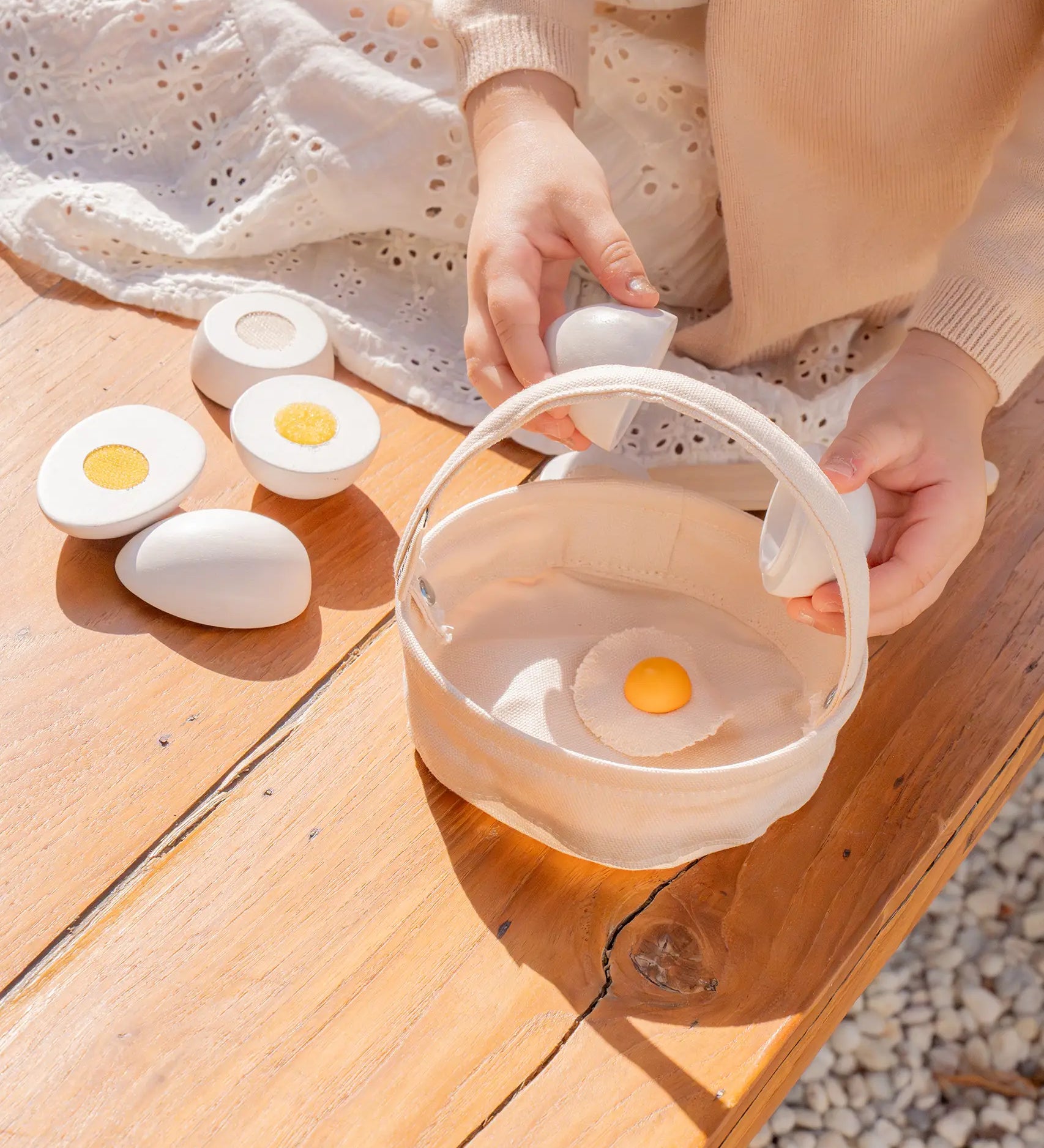 Child holding a Plantoys wooden play egg above a fabric basket on a wooden bench