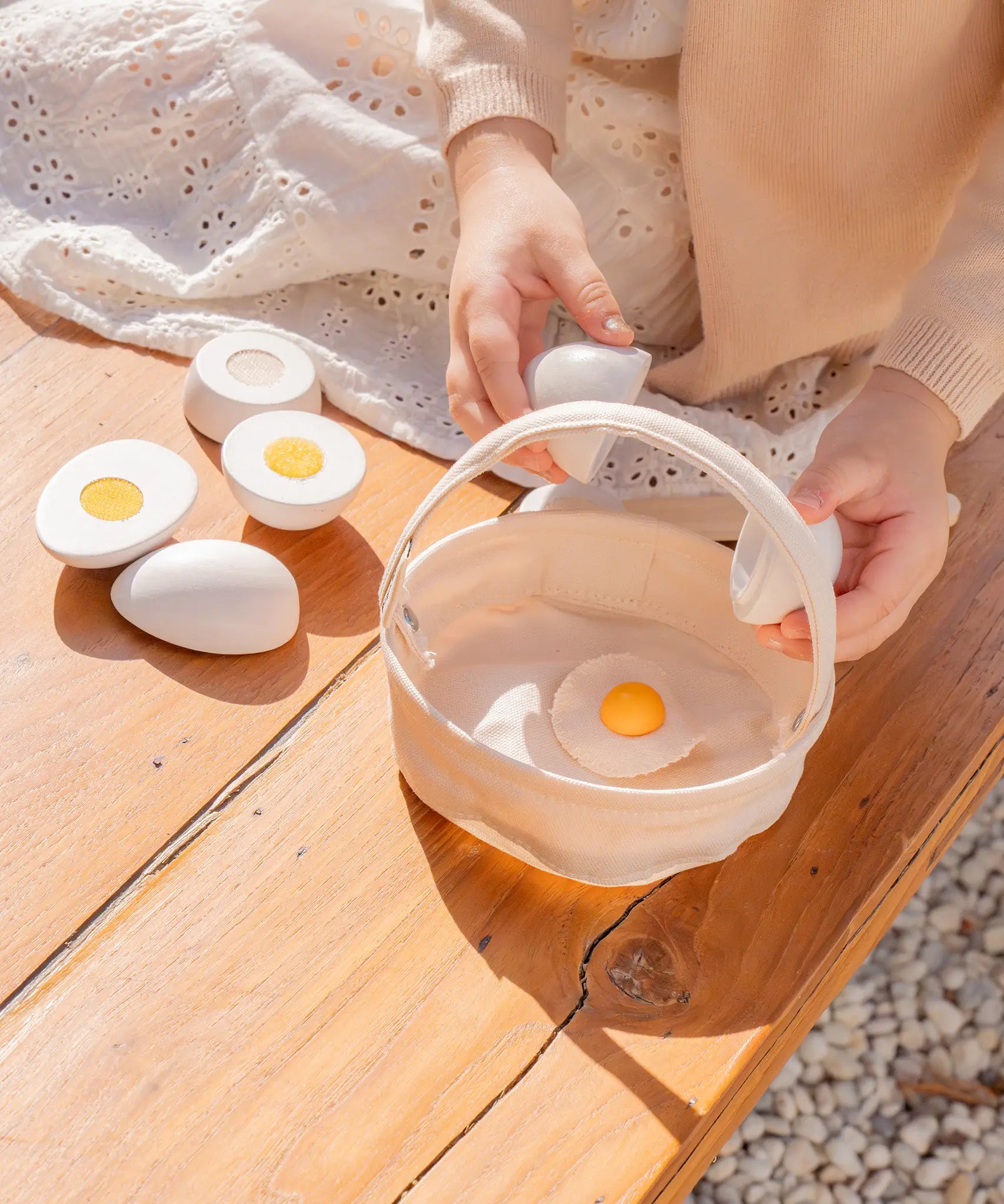 Child holding a Plantoys wooden play egg above a fabric basket on a wooden bench