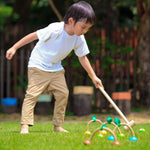 A child playing with the PlanToys Croquet set outdoors on a lawn. 
