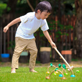 A child playing with the PlanToys Croquet set outdoors on a lawn. 