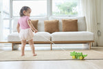 Baby girl pulling the Plan Toys Dancing Alligator wooden pull along toy across a living room floor