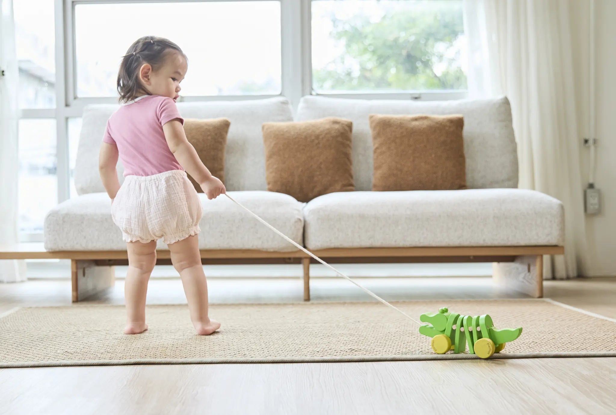 Baby girl pulling the Plan Toys Dancing Alligator wooden pull along toy across a living room floor