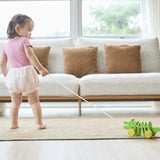 Baby girl pulling the Plan Toys Dancing Alligator wooden pull along toy across a living room floor