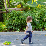 Toddler pulling the Plan Toys Dancing Alligator wooden pull along toy along an outdoor garden path