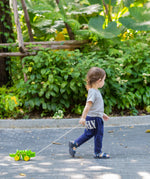 Toddler pulling the Plan Toys Dancing Alligator wooden pull along toy along an outdoor garden path