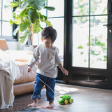 Toddler walking indoors pulling the Plan Toys Dancing Alligator wooden pull along toy across a wood floor